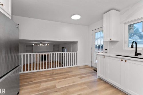 Kitchen featuring white shaker cabinetry, light wood-finish flooring, a stainless steel refrigerator, and a black gooseneck faucet - 3208 130 Avenue, Edmonton, AB - Indoor Photo Showing Other Room