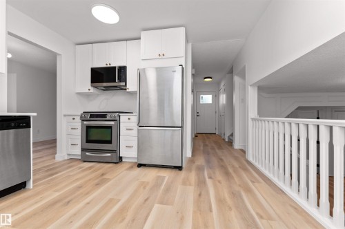 Kitchen area featuring stainless steel appliances, white cabinetry, and wood-finish flooring - 3208 130 Avenue, Edmonton, AB - Indoor Photo Showing Kitchen