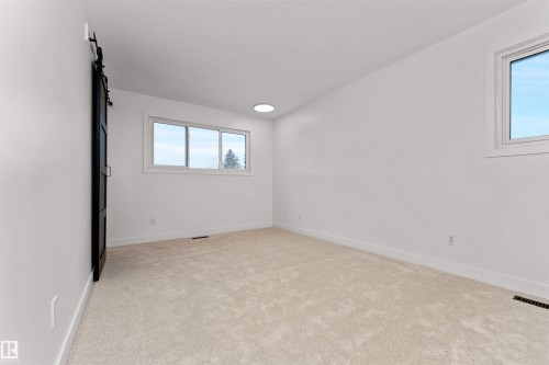 Light beige carpeted room featuring a modern black barn door, three white-framed windows, recessed circular lighting, and white walls - 3208 130 Avenue, Edmonton, AB - Indoor Photo Showing Other Room