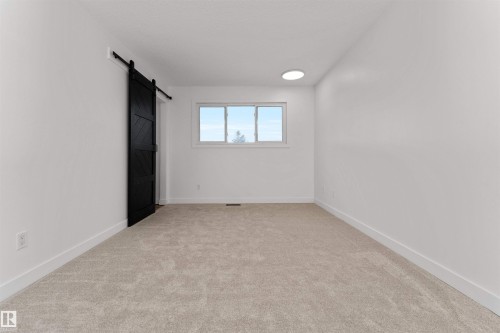 Spacious room featuring light-toned carpeting, white walls, and a black barn door - 3208 130 Avenue, Edmonton, AB - Indoor Photo Showing Other Room