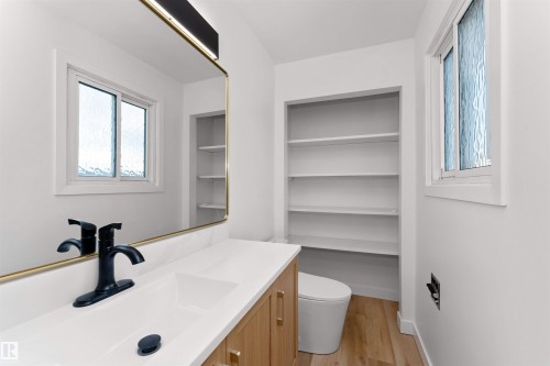 Contemporary bathroom featuring a light wood-finish vanity with gold-tone hardware, a white countertop with an integrated sink, and a matte black faucet - 3208 130 Avenue, Edmonton, AB - Indoor Photo Showing Bathroom