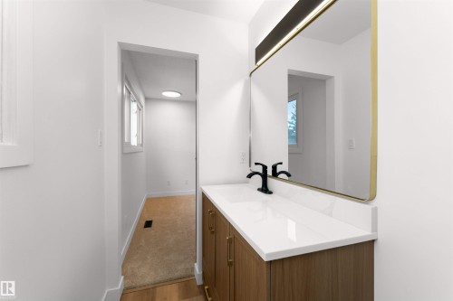 Bathroom vanity featuring a quartz countertop, matte black faucet, and a gold-framed mirror with integrated lighting - 3208 130 Avenue, Edmonton, AB - Indoor Photo Showing Bathroom