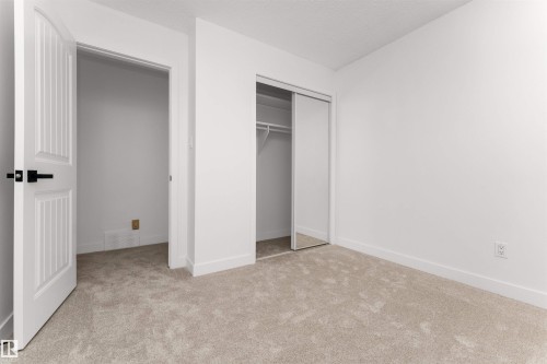 Neutral-toned carpeted room featuring a white interior door with black hardware, a built-in closet with mirrored sliding doors, and white baseboards - 3208 130 Avenue, Edmonton, AB - Indoor Photo Showing Other Room