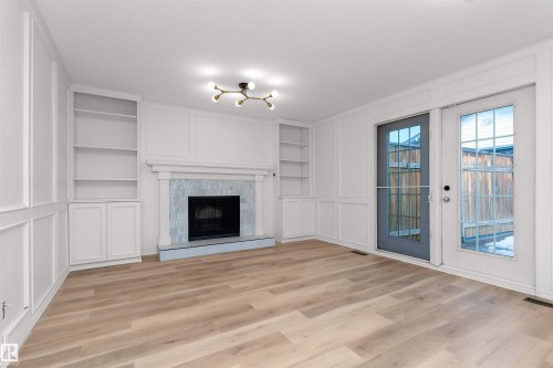 Living area featuring a fireplace with a light-toned tile surround and dark hearth, built-in shelving, wood-finish flooring, and white paneled walls - 3208 130 Avenue, Edmonton, AB - Indoor Photo Showing Living Room With Fireplace