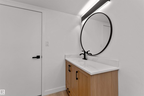 Modern vanity featuring a light wood-finish cabinet with black pulls, a white countertop, and a black circular mirror - 3208 130 Avenue, Edmonton, AB - Indoor
