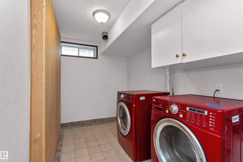 Utility area featuring a window, overhead lighting, white cabinetry with gold-toned hardware, and tiled flooring - 3208 130 Avenue, Edmonton, AB - Indoor Photo Showing Laundry Room
