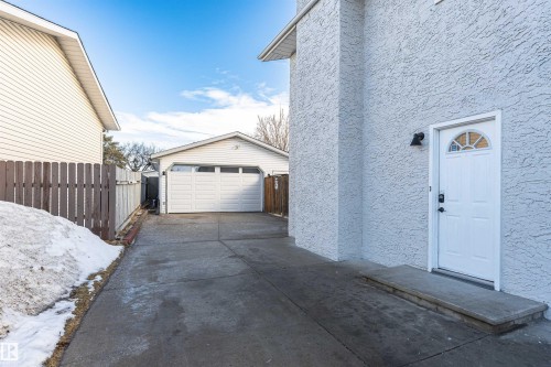 Side access door with an exterior sconce, stucco siding, and a concrete pathway - 3208 130 Avenue, Edmonton, AB - Outdoor With Exterior