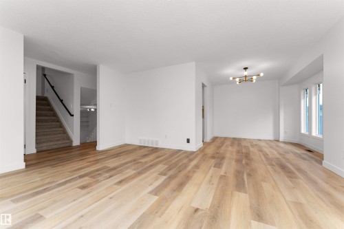 Spacious interior featuring wide plank wood-finish flooring, white walls, and a modern multi-bulb chandelier - 3208 130 Avenue, Edmonton, AB - Indoor Photo Showing Other Room