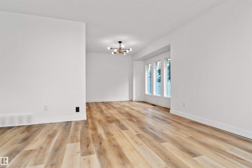 Expansive room featuring wood-finish flooring, crisp white walls, and a contemporary multi-arm chandelier - 3208 130 Avenue, Edmonton, AB - Indoor Photo Showing Other Room
