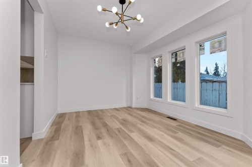 Spacious room featuring light wood-finish flooring, a contemporary black and gold chandelier, and three large windows providing ample natural light - 3208 130 Avenue, Edmonton, AB - Indoor Photo Showing Other Room