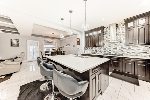 Gourmet kitchen with dark wood cabinetry, a mosaic tile backsplash, and a large central island featuring a white countertop and seating - 69 Caragana Way, Fort Saskatchewan, AB 