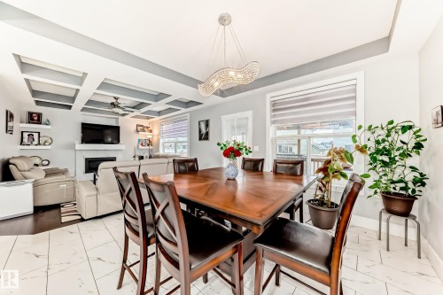 Open-concept living and dining areas featuring coffered ceilings, a central ceiling fan, and a fireplace with a white mantel - 69 Caragana Way, Fort Saskatchewan, AB 