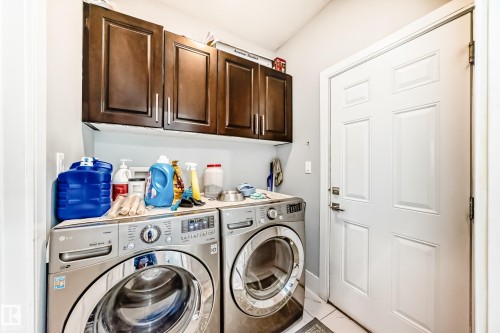 Dedicated laundry area featuring dark wood-finish cabinetry, a built-in utility sink, and white tile flooring - 69 Caragana Way, Fort Saskatchewan, AB 