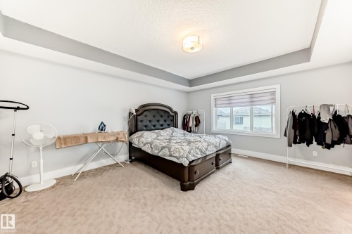 Spacious bedroom featuring light neutral carpet, tray ceiling with recessed lighting, and a window with blinds - 69 Caragana Way, Fort Saskatchewan, AB 