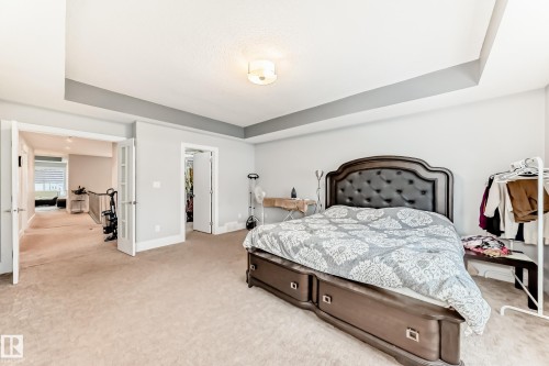 Carpeted bedroom featuring a tray ceiling, recessed lighting, and a doorway opening to a hallway with a railing - 69 Caragana Way, Fort Saskatchewan, AB 