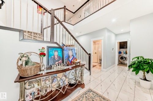 Two-story entryway featuring a dark wood staircase with metal balusters, white tile flooring, and integrated ceiling lighting - 69 Caragana Way, Fort Saskatchewan, AB 