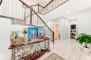 Two-story entryway featuring a dark wood staircase with metal balusters, white tile flooring, and integrated ceiling lighting - 69 Caragana Way, Fort Saskatchewan, AB 