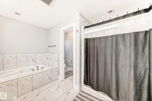 Bathroom featuring a soaking tub with integrated deck, white tile surround, and a walk-in shower with clear glass enclosure - 69 Caragana Way, Fort Saskatchewan, AB 