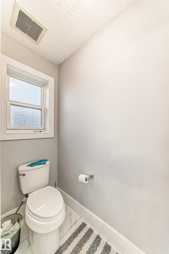 Bathroom featuring a white toilet, frosted window, ceiling ventilation fan, and light gray walls - 69 Caragana Way, Fort Saskatchewan, AB 