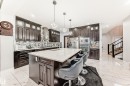 Modern kitchen featuring dark wood-finish cabinetry, a large center island with a light-toned countertop, stainless steel appliances, and a geometric tile backsplash - 69 Caragana Way, Fort Saskatchewan, AB 