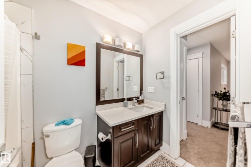 Bathroom featuring a dark wood vanity with a light-colored countertop, an undermount sink, and a framed mirror with a four-light fixture - 69 Caragana Way, Fort Saskatchewan, AB 