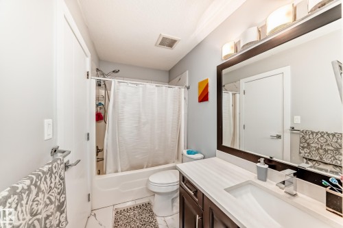 Bathroom featuring a single vanity with a white countertop, an integrated rectangular sink, a dark wood-finish cabinet, and a large framed mirror - 69 Caragana Way, Fort Saskatchewan, AB 