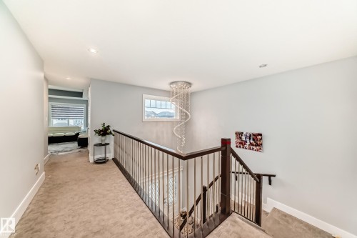 Carpeted upper-level landing featuring a white wall palette, recessed lighting, dark wood handrails with metal balusters, and a contemporary crystal chandelier - 69 Caragana Way, Fort Saskatchewan, AB 