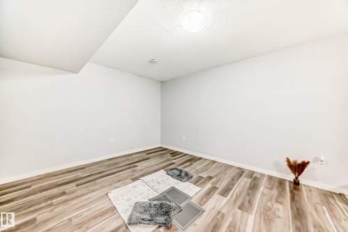 Spacious room featuring wood-finish flooring, light neutral wall paint, and a ceiling-mounted light fixture - 69 Caragana Way, Fort Saskatchewan, AB 