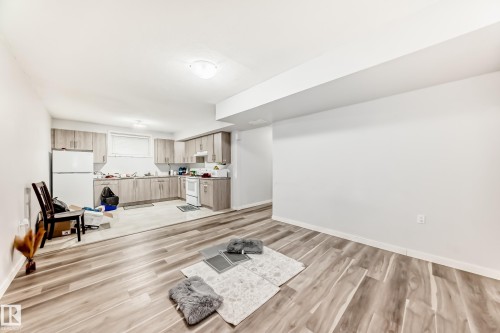 Open-concept living space featuring wood-finish flooring, a contemporary kitchen with light-toned cabinetry, and white appliances - 69 Caragana Way, Fort Saskatchewan, AB 