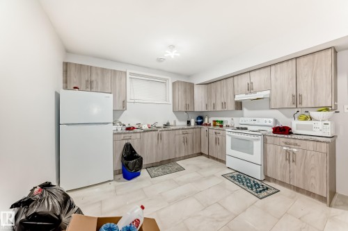 Kitchen featuring wood-finish cabinetry, light-toned countertops, and a full suite of white appliances - 69 Caragana Way, Fort Saskatchewan, AB 