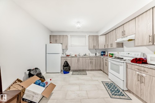 Kitchen featuring light wood-finish cabinetry, light-toned countertops, and a white electric range with a coordinating range hood - 69 Caragana Way, Fort Saskatchewan, AB 
