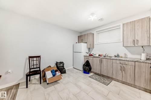 Kitchenette featuring wood-grain cabinetry, light granite-style countertops, stainless steel sink, and white appliances - 69 Caragana Way, Fort Saskatchewan, AB 