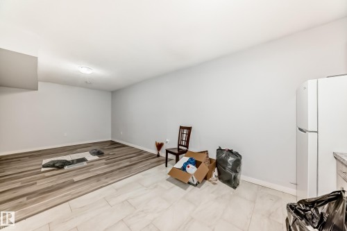 Spacious room featuring light gray walls, a flush-mount ceiling light, and a combination of wood-finish flooring and light-toned tile flooring - 69 Caragana Way, Fort Saskatchewan, AB 