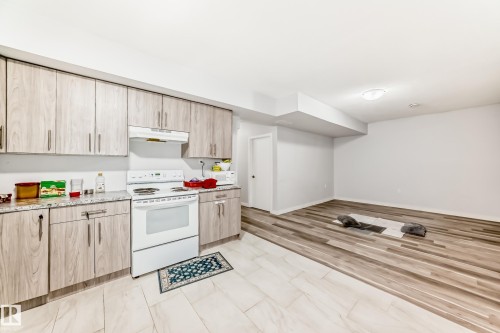 Kitchen area featuring light wood-finish cabinetry, speckled countertops, and a white electric range with overhead ventilation - 69 Caragana Way, Fort Saskatchewan, AB 