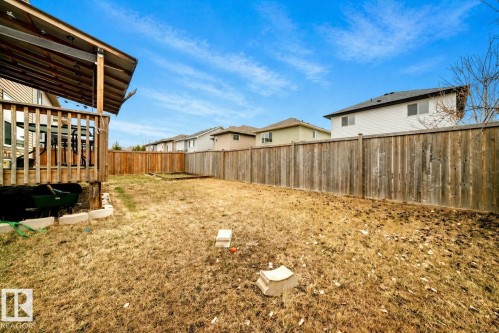 Expansive backyard featuring a full-height wood privacy fence, a covered wooden deck with railings, and established neighboring properties - 69 Caragana Way, Fort Saskatchewan, AB 