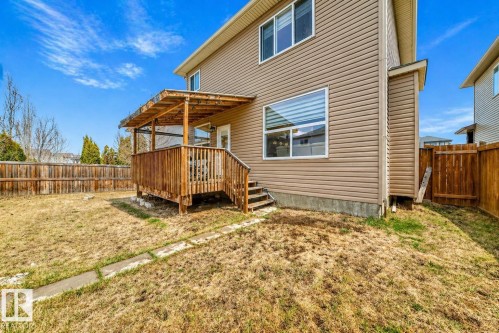 Expansive backyard featuring a covered wood deck with railing, a privacy fence, and a concrete paver pathway - 69 Caragana Way, Fort Saskatchewan, AB 