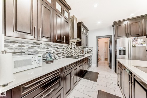 Contemporary kitchen featuring dark wood cabinetry, light countertops, patterned tile backsplash, stainless steel appliances, and recessed lighting - 69 Caragana Way, Fort Saskatchewan, AB 
