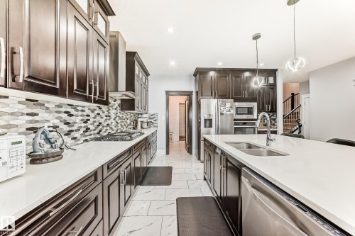 Modern kitchen featuring dark wood cabinetry, stainless steel appliances, white countertops, and a patterned tile backsplash - 69 Caragana Way, Fort Saskatchewan, AB 