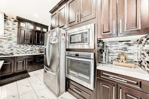 Kitchen featuring dark wood-finish cabinetry, stainless steel appliances, a mosaic tile backsplash, white countertops, and tile flooring - 69 Caragana Way, Fort Saskatchewan, AB 
