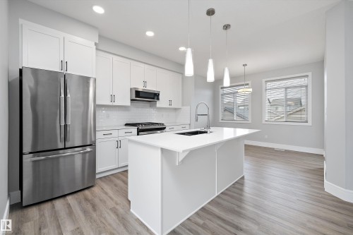 Contemporary kitchen featuring an expansive island with a waterfall edge, stainless steel appliances, white shaker cabinetry, pendant lighting, and wood-finish flooring - 4235 Chichak Close, Edmonton, AB - Indoor Photo Showing Kitchen With Upgraded Kitchen