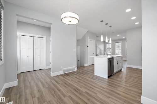 Open-concept living area featuring wood-finish flooring, recessed lighting, a kitchen island with pendant lighting, and modern bi-fold closet doors - 4235 Chichak Close, Edmonton, AB - Indoor Photo Showing Kitchen With Upgraded Kitchen
