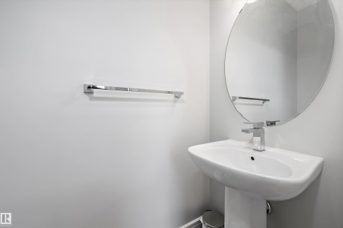 Pedestal sink with a contemporary chrome faucet, complemented by a large oval mirror and modern chrome towel bar - 4235 Chichak Close, Edmonton, AB - Indoor Photo Showing Bathroom