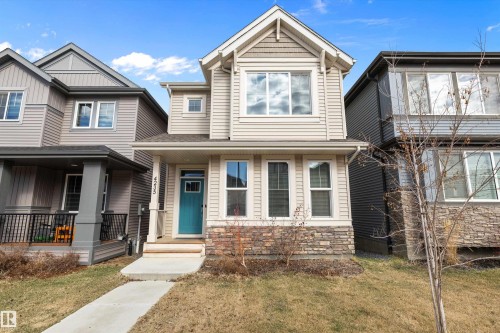 Contemporary residence featuring light-toned siding, a vibrant teal front door, and a stone-clad foundation - 4235 Chichak Close, Edmonton, AB - Outdoor With Facade