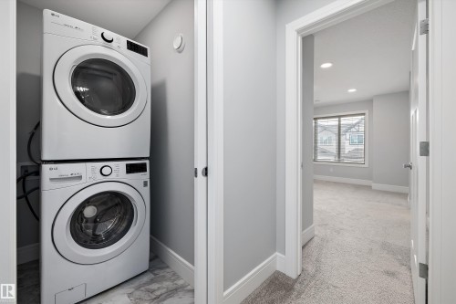 Stackable front-load washer and dryer set within a dedicated alcove featuring marble-finish flooring - 4235 Chichak Close, Edmonton, AB - Indoor Photo Showing Laundry Room
