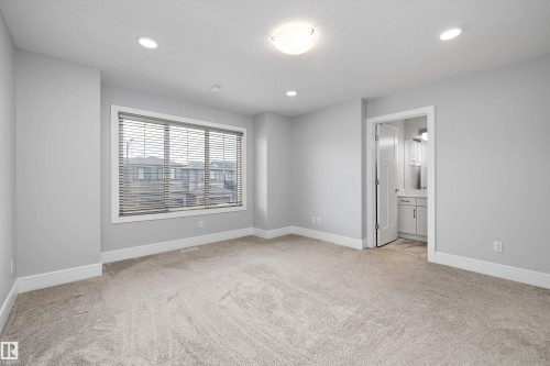 Spacious interior featuring neutral carpeting, light gray walls, white baseboards, and a large window with blinds - 4235 Chichak Close, Edmonton, AB - Indoor Photo Showing Other Room