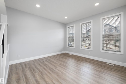 Spacious room featuring light wood-finish flooring, recessed ceiling lighting, three windows with blinds, and white trim throughout - 4235 Chichak Close, Edmonton, AB - Indoor Photo Showing Other Room