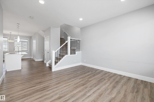 Open-concept living space featuring wood-finish flooring, recessed lighting, and a staircase with white balusters and dark metal spindles - 4235 Chichak Close, Edmonton, AB - Indoor Photo Showing Other Room