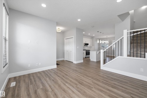 Open-concept living space featuring wood-finish flooring, recessed lighting, and a prominent staircase with black metal balusters - 4235 Chichak Close, Edmonton, AB - Indoor Photo Showing Other Room