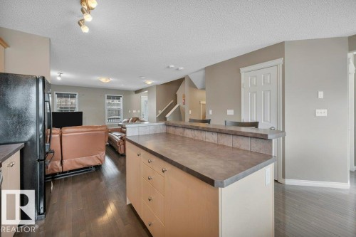 Kitchen island featuring a laminate countertop, integrated cabinetry, and a tile-faced breakfast bar - 12063 19 Avenue, Edmonton, AB - Indoor Photo Showing Kitchen
