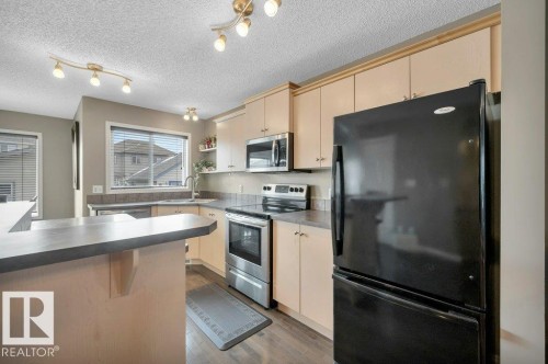 Kitchen featuring light-tone cabinetry, a breakfast bar, and stainless steel appliances - 12063 19 Avenue, Edmonton, AB - Indoor Photo Showing Kitchen